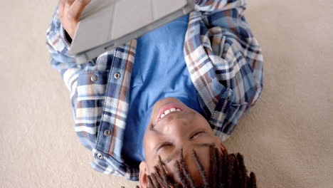 Glücklicher-Afroamerikanischer-Junge-Mit-Tablet,-Das-Zu-Hause-Auf-Dem-Boden-Liegt,-Zeitlupe
