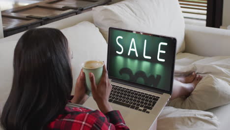 Biracial-woman-on-couch-with-coffee,-using-laptop-for-online-shopping,-slow-motion