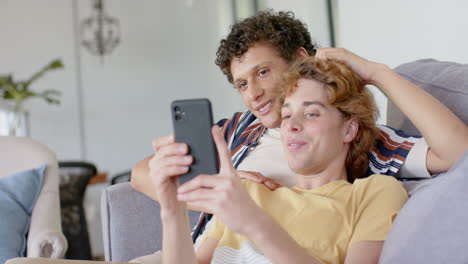 Happy-diverse-gay-male-couple-sitting-at-sofa-using-smartphone-at-home,-slow-motion
