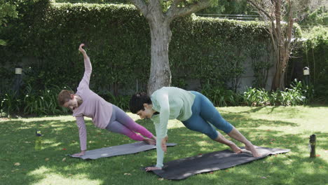 Happy-caucasian-lesbian-couple-practising-yoga-in-sunny-garden,-slow-motion