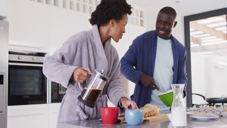 Video-of-happy-african-american-couple-preparing-breakfast-and-coffee-in-kitchen