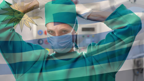 Animation-of-waving-uruguay-flag-against-caucasian-female-surgeon-wearing-surgical-mask-at-hospital