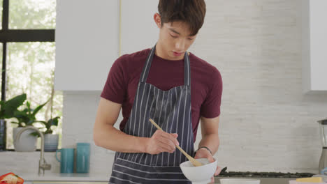 Asian-male-teenager-preparing-food-and-wearing-apron-in-kitchen