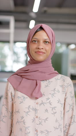 Vertical-video-of-portrait-of-happy-biracial-casual-businesswoman-in-hijab-in-office,-slow-motion