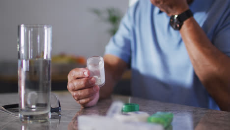 Senior-biracial-man-with-glass-of-water-taking-pills