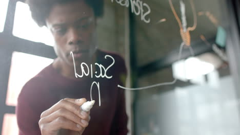 African-american-casual-businessman-writing-on-glass-wall-at-home-office,-copy-space,-slow-motion