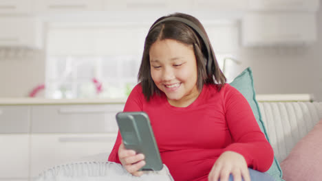 Video-Eines-Glücklichen-Asiatischen-Mädchens,-Das-Mit-Seinem-Smartphone-Auf-Dem-Sofa-Ruht
