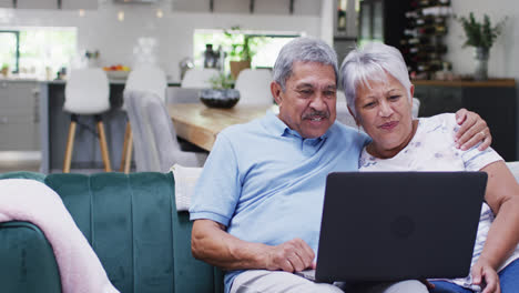 Happy-senior-biracial-couple-laughing-and-using-tablet