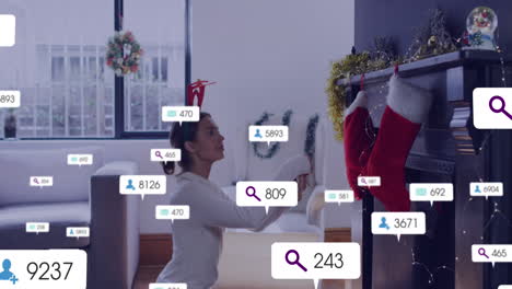 Animation-of-social-media-icons-with-numbers-over-caucaisian-woman-decorating-house-for-christmas