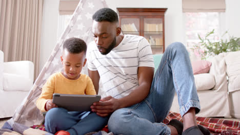Glücklicher-Afroamerikanischer-Vater-Und-Sohn,-Die-Ein-Tablet-Benutzen-Und-Zu-Hause-Lächeln,-Zeitlupe