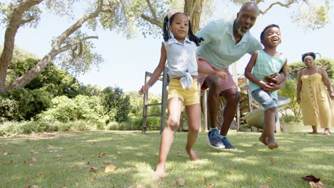 Glückliche-Afroamerikanische-Großeltern-Mit-Enkelkindern,-Die-Im-Garten-Fußball-Spielen,-In-Zeitlupe