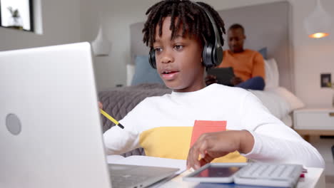 African-american-boy-using-laptop-for-online-lesson-with-father-in-background-at-home,-slow-motion