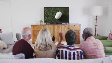 Senior-diverse-friends-watching-tv-with-rugby-ball-at-stadium-on-screen