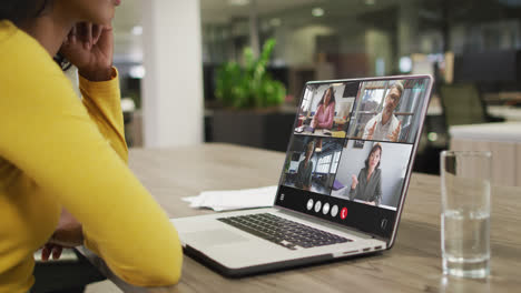 Biracial-woman-using-laptop-for-video-call,-with-diverse-business-colleagues-on-screen