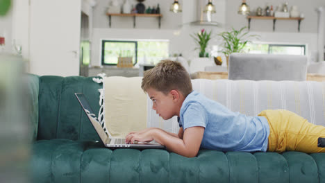 Glücklicher-Kaukasischer-Junge,-Der-Auf-Dem-Sofa-Liegt-Und-Einen-Laptop-Benutzt,-Zeitlupe