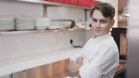 Portrait-of-caucasian-male-chef-with-crossed-arms-and-smiling-in-kitchen,-copy-space,-slow-motion