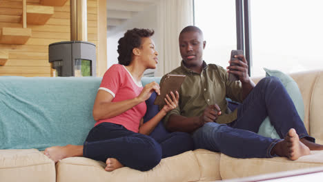 Video-of-happy-african-american-couple-sitting-on-sofa-and-using-tablet