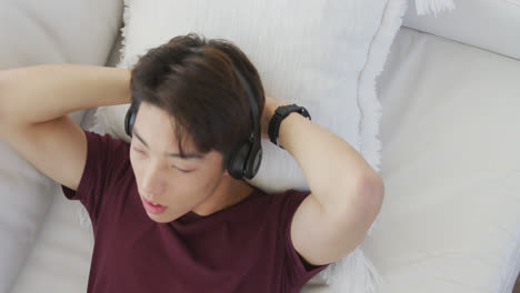 Asian-male-teenager-listening-to-music-with-headphones-in-living-room