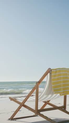 Vertical-video-of-deck-chair-and-towel-on-beach,-in-slow-motion,-with-copy-space