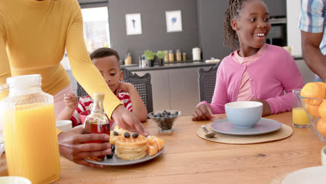 African-american-parents-with-son-and-daughter-serving-breakfast-at-table-in-kitchen,-slow-motion