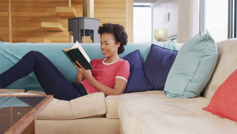 Video-of-african-american-woman-reading-book-on-sofa