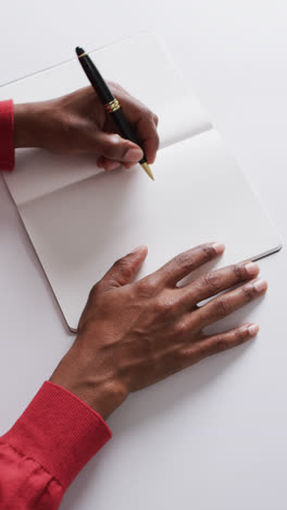 Vertical-video-of-hand-writing-with-pen-on-book-with-copy-space-on-white-background-in-slow-motion