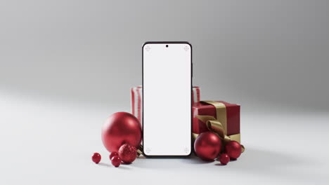 Video-of-christmas-presents,-baubles-and-smartphone-with-copy-space-on-white-background