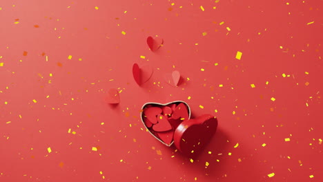 Animation-Von-Gelbem-Konfetti,-Das-über-Herzförmige-Papierausschnitte-In-Einer-Herzförmigen-Schachtel-Auf-Rotem-Hintergrund-Fällt