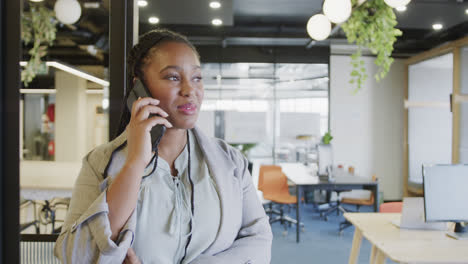 Happy-african-american-casual-businesswoman-talking-on-smartphone-standing-in-office,-slow-motion