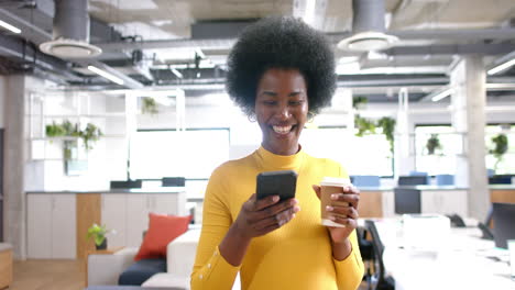Happy-african-american-casual-businesswoman-walking-and-using-smartphone-in-office,-slow-motion