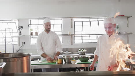 Group-of-focused-diverse-male-chefs-preparing-meals-with-bursting-fire-in-kitchen,-slow-motion