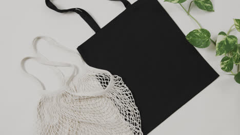 Close-up-of-white-and-black-bags-with-green-plant-on-white-background,-with-copy-space,-slow-motion