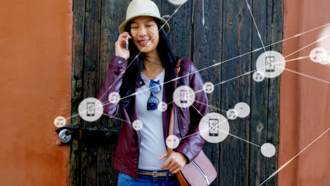 Animation-of-network-of-connections-with-icons-over-asian-woman-talking-on-smartphone