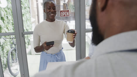 Mujer-Afroamericana-Sonriente-Pagando-Café-Para-Llevar-En-Una-Cafetería-Con-Teléfono-Inteligente,-Cámara-Lenta