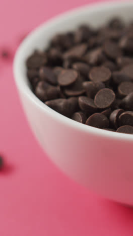 Video-of-close-up-of-bowl-of-chocolate-chip-over-pink-background