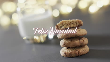 Feliz-navidad-text-in-white-over-christmas-cookies,-milk-and-bokeh-lights