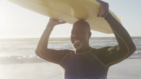 Portrait-of-happy-senior-african-american-man-holding-surfboard-at-beach,-in-slow-motion