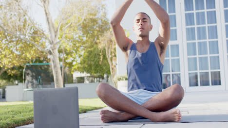 Fokussierter-Biracial-Mann,-Der-Yoga-Mit-Laptop-Im-Sonnigen-Garten-Praktiziert,-Zeitlupe