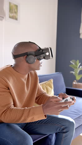 Vertical-video-of-african-american-man-using-vr-headset-and-playing-video-games-at-home,-slow-motion