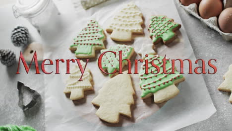 Merry-christmas-text-in-red-over-decorated-christmas-cookies-and-on-kitchen-worktop