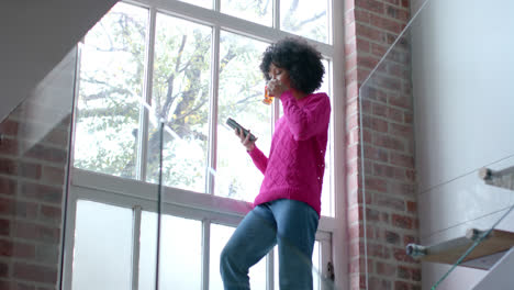 Biracial-woman-drinking-tea-and-using-smartphone-at-home,-slow-motion