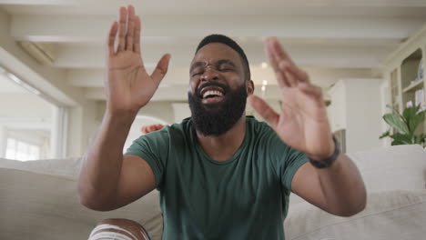 An-African-American-man-laughs-on-a-couch-in-a-cozy-room-on-a-video-call