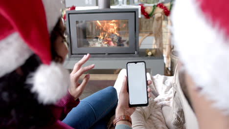 Biracial-couple-wearing-santa-hats-using-smartphone-with-copy-space-on-screen-at-home,-slow-motion
