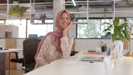 Glückliche-Gemischtrassige-Geschäftsfrau-Im-Hijab-Mit-Laptop-Im-Büro,-Zeitlupe