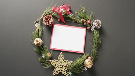 Video-of-christmas-wreath-decorations-and-white-card-with-copy-space-on-black-background