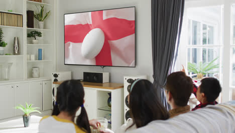 Asian-family-watching-tv-with-rugby-ball-on-flag-of-england-on-screen