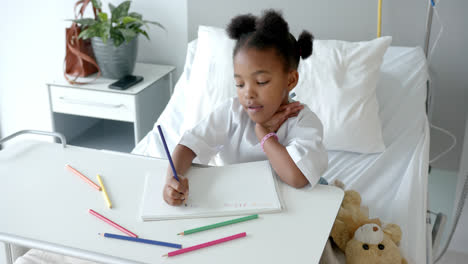 African-american-girl-drawing-in-notebook-in-hospital-bed,-slow-motion