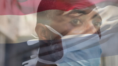 Animation-of-waving-netherlands-flag-against-african-american-man-in-face-mask-on-the-street