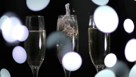 Animation-of-white-spots-falling-over-champagne-glasses-on-black-background