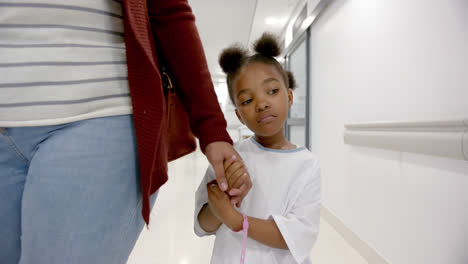 Afroamerikanische-Mutter-Und-Tochter-Im-Krankenhauskleid-Halten-Händchen-Beim-Gehen-Im-Flur,-Zeitlupe